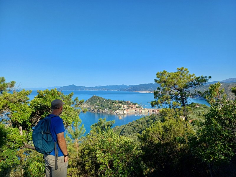 Cinque volontari sorridono sul sentiero con gerle cariche di materiale, il mare alle spalle.